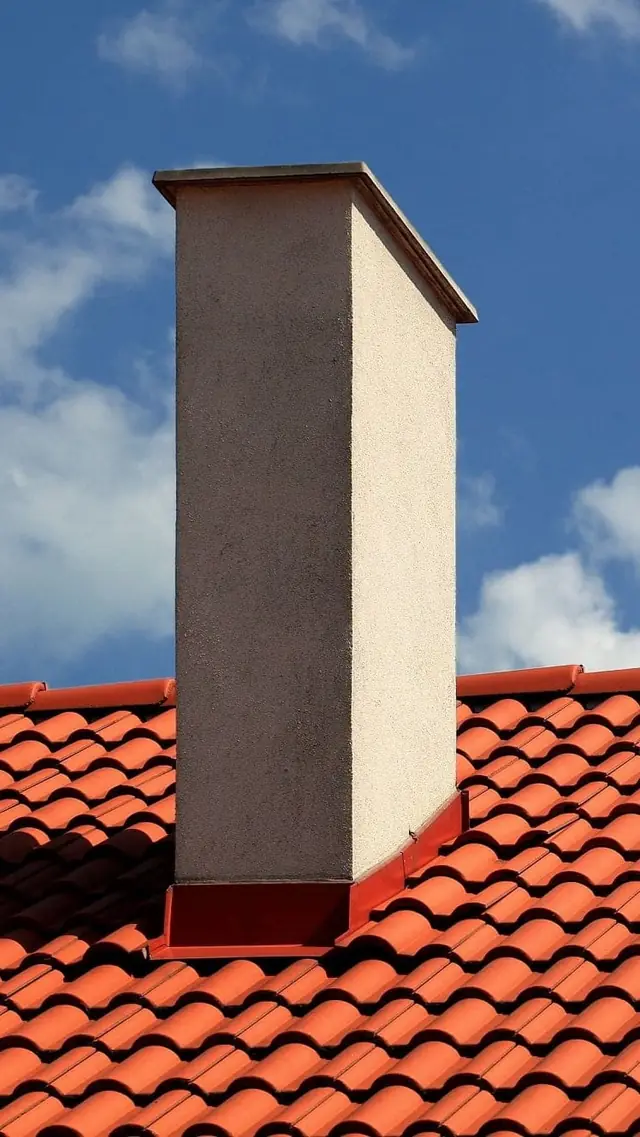 Verputzter Kamin auf einem roten Ziegeldach unter blauem Himmel